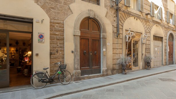 A stone building with a wooden door and a bicycle parked outside. - Santo Spirito Venti (Florence)