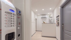 A modern hotel corridor with a self-service coffee machine, a kitchen area, and a door to a room. - Santo Spirito Venti (Florence)