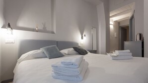 A neatly made bed with white linens, a grey headboard, and a stack of folded towels on the bed. - Santo Spirito Venti (Florence)