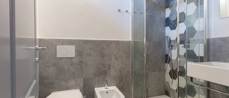 Un baño moderno con cabina de ducha de vidrio, un bidé y un inodoro.