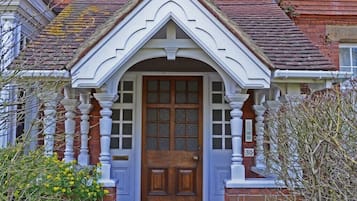 Uma casa tradicional com uma porta frontal imponente, fachada de tijolos e varanda decorativa com balaústres brancos.