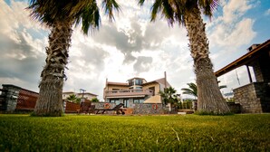 A modern house with a stone facade, a balcony, and a well-maintained lawn with palm trees. - Villa Theano - 4 bedroom villa close to the beach (Agios Nikolaos)