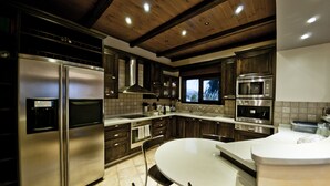 A modern kitchen with stainless steel appliances, wooden cabinets, and a large island with seating. - Villa Theano - 4 bedroom villa close to the beach (Agios Nikolaos)