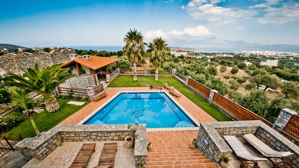 A swimming pool with a stone deck, surrounded by a stone wall and a wooden deck with lounge chairs. - Villa Theano - 4 bedroom villa close to the beach (Agios Nikolaos)