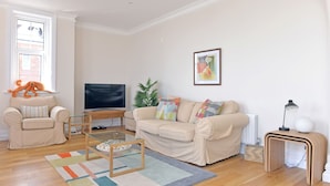 A living room with a beige sofa, a glass coffee table, a television, and a lamp. - Sea Dreams (Eastbourne)