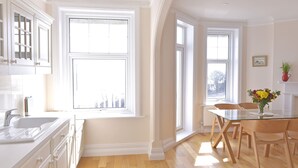 A bright kitchen with white cabinetry, a wooden dining table, and a vase of flowers. - Sea Dreams (Eastbourne)