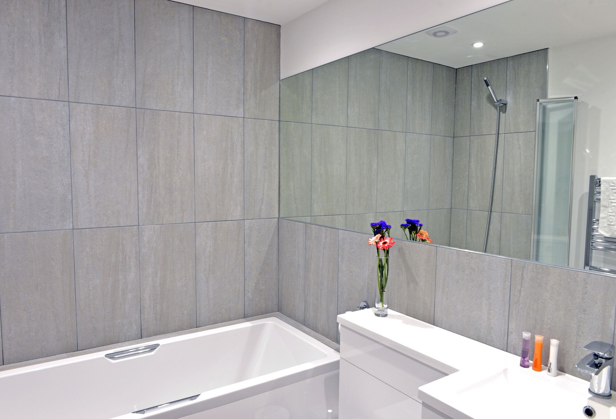 Ein modernes Badezimmer mit einem großen Spiegel, einer Badewanne und einem weißen Waschtisch mit Toilettenartikeln.