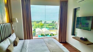 A hotel room with a bed, a TV on the wall, and a window with a view of greenery and buildings. - Grace Cox Smart Hotel (Cox's Bazar)