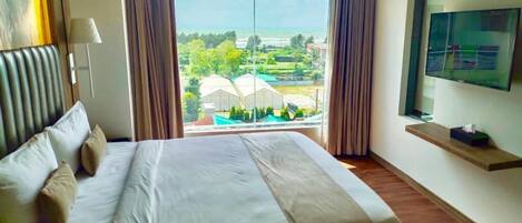 A hotel room with a bed, a TV on the wall, and a window with a view of greenery and buildings.