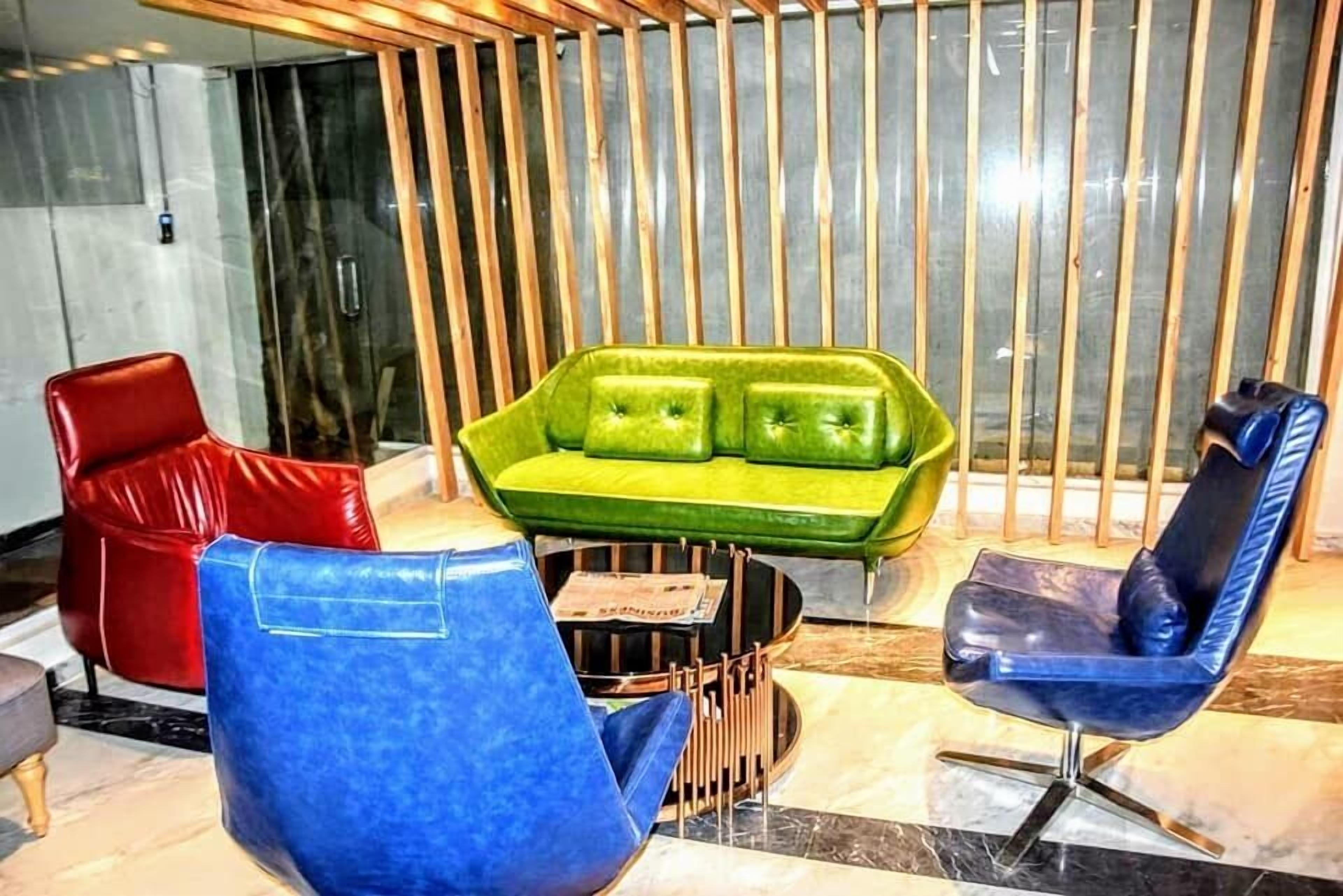 A modern interior with a green sofa, red and blue chairs, and a wooden slatted wall.
