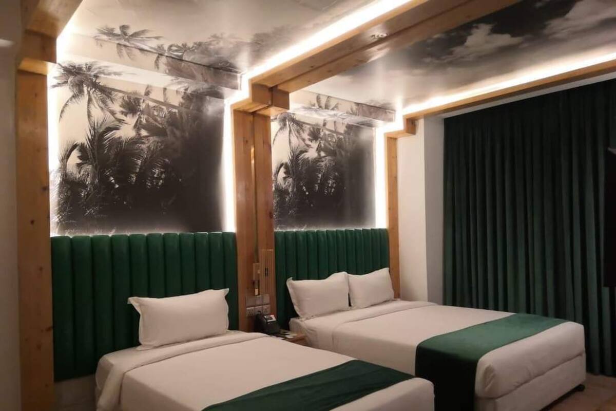 A hotel room with two beds, green headboards, and a mural of palm trees on the wall.