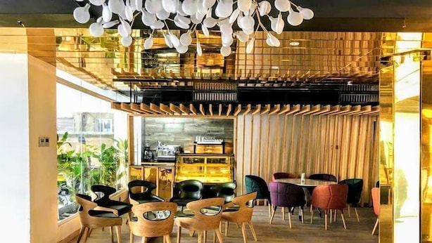 A modern interior with wooden paneling, a variety of seating options including round tables and chairs, and a visible kitchen area in the background. - Grace Cox Smart Hotel (Cox's Bazar)