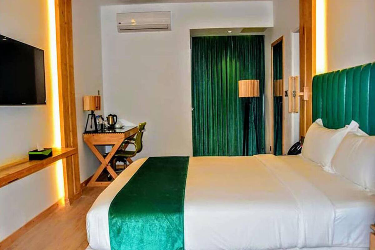 A hotel room with a large bed, a desk with a chair, a television mounted on the wall, and a green curtain.