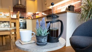 Una cafetera, una taza y una planta en maceta sobre una mesa redonda pequeña en una cocina.