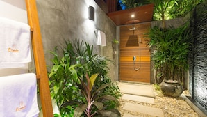 Entrada de um spa, com parede de concreto, porta de madeira e plantas em vasos.