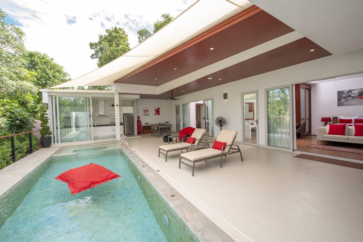 Een modern huis met een zwembad, twee loungesteilen en een eethoek.