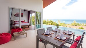 Uma área de refeições com uma mesa posta para quatro pessoas, uma poltrona de couro vermelho e vista para o oceano.