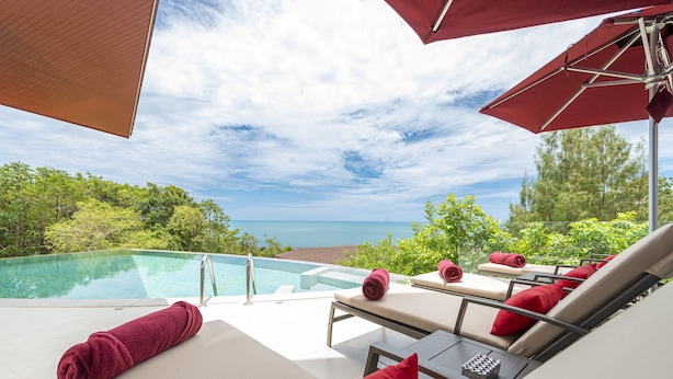 Uma área junto à piscina com espreguiçadeiras e guarda-sóis, com vista para um céu azul límpido e uma piscina.