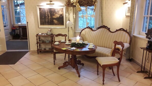 A dining area with a round table, two chairs, a sofa, and a painting on the wall.