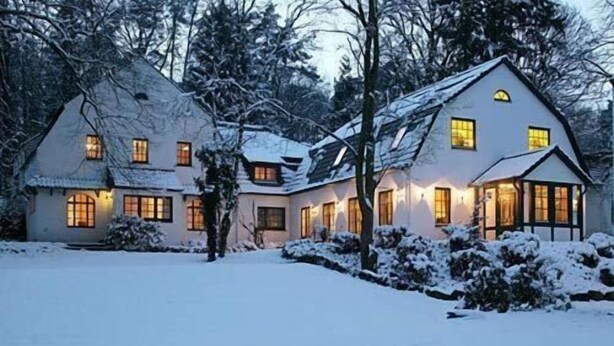A two-story house with a snow-covered roof and a well-lit front porch. - Hotel Buchenhof (Worpswede)