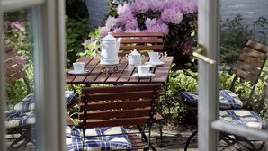 An outdoor patio with a wooden table set for tea, surrounded by benches with blue and white cushions. - Hotel Buchenhof (Worpswede)