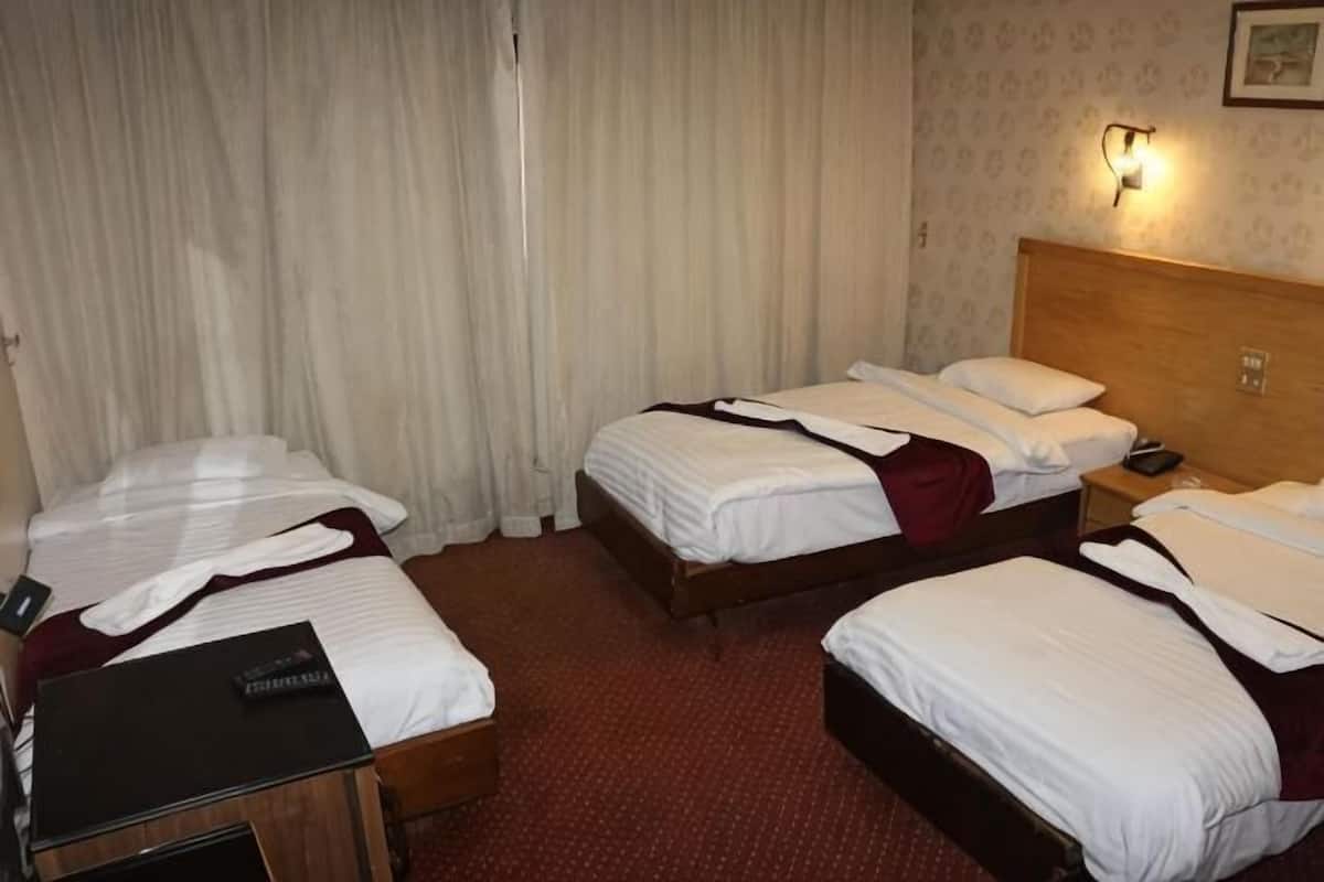 A hotel room with two beds, a wooden headboard, a nightstand, and a curtain.