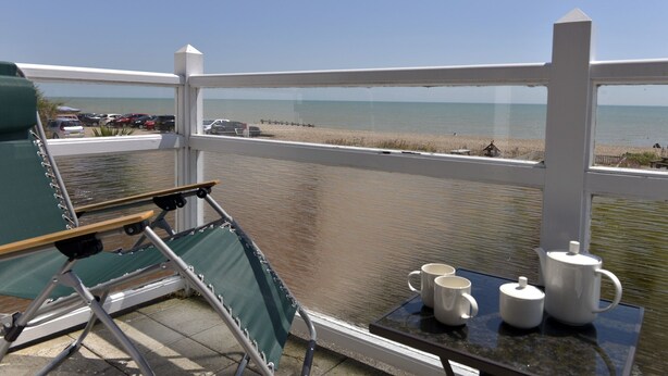 A balcony with a view of the beach, a folding chair, and a table with two mugs and a teapot. - Beach Garden (Pevensey)