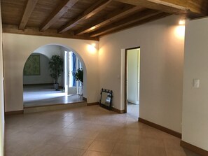 A spacious hallway with a tiled floor, wooden beams on the ceiling, and a large arched doorway leading to another room.