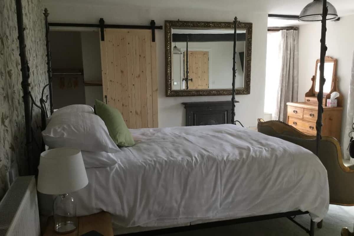 A bedroom with a bed, a nightstand with a lamp, a dresser, and a mirror.