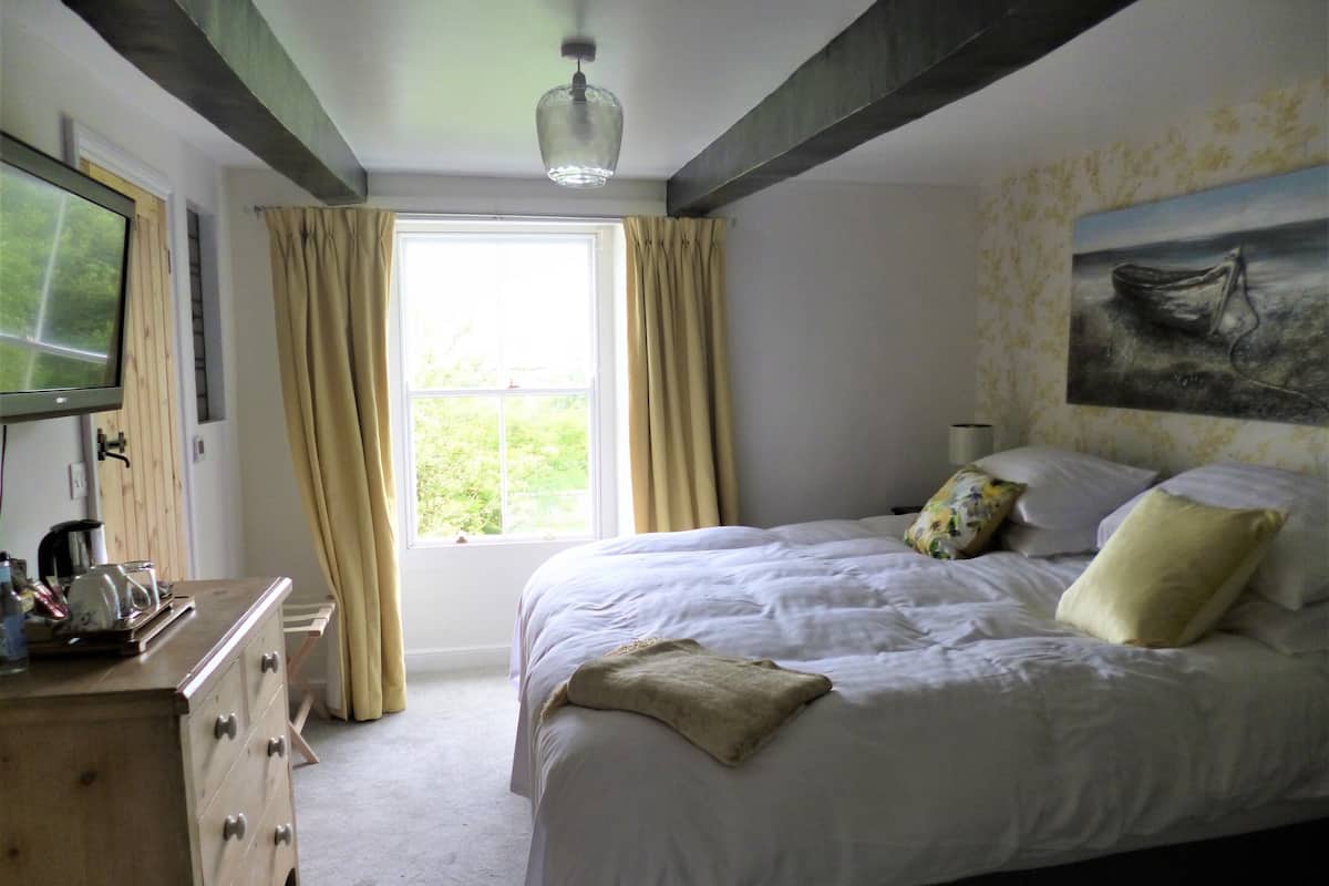 A bedroom with a bed, a dresser, a television, and a window with curtains.