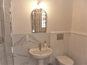 A bathroom with a marble-tiled wall, a white sink with a mirror above it, and a toilet. - The Burrows Bed and Breakfast (Pembroke)