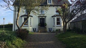 A two-story house with a front entrance, a gravel driveway, and a garden with various plants and a tree. - The Burrows Bed and Breakfast (Pembroke)