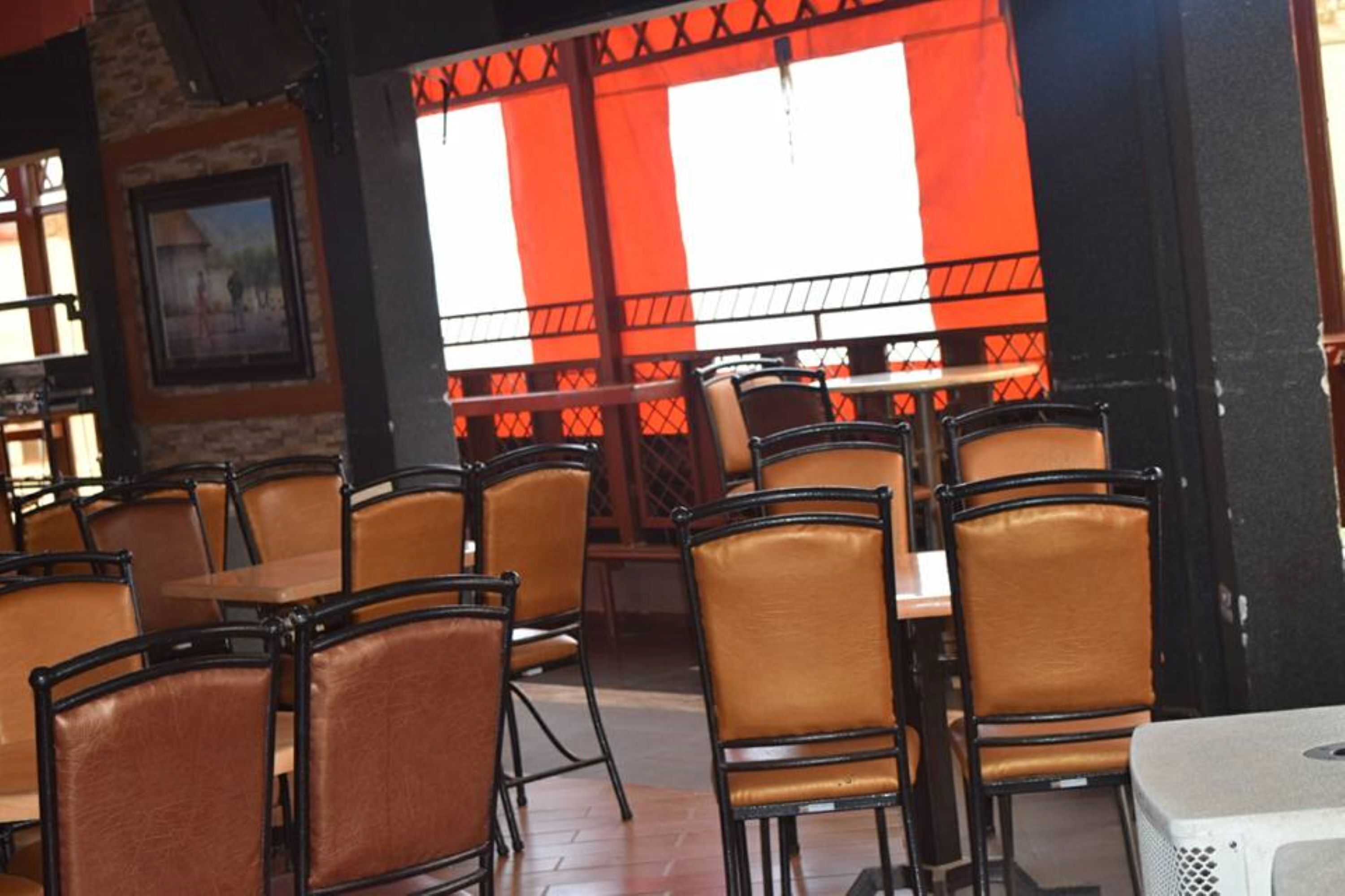 Un espace de restauration intérieur avec des tables et des chaises, un mur en briques et une fenêtre ornée d’un store à rayures rouges et blanches.
