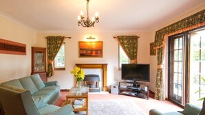 A living room with two sofas, a TV, a fireplace, and a large window with curtains. - Cottage at Friston Down (Eastbourne)