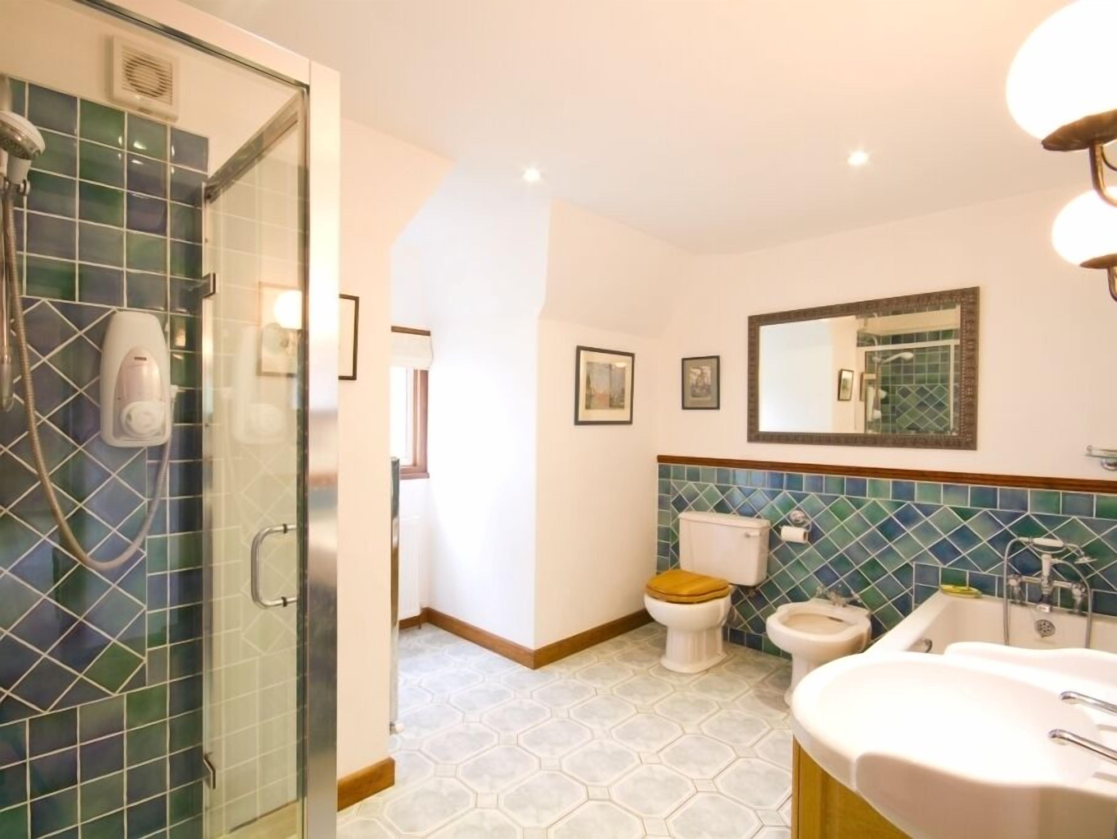 A bathroom with a glass shower enclosure, two toilets, a sink, and a mirror.