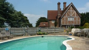 A swimming pool with a stone deck, surrounded by a wooden fence and a brick house in the background. - Cottage at Friston Down (Eastbourne)
