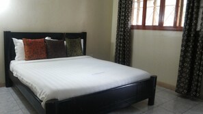 A neatly made bed with a white sheet and multiple pillows in various patterns. - Dich Comfort (Gulu)