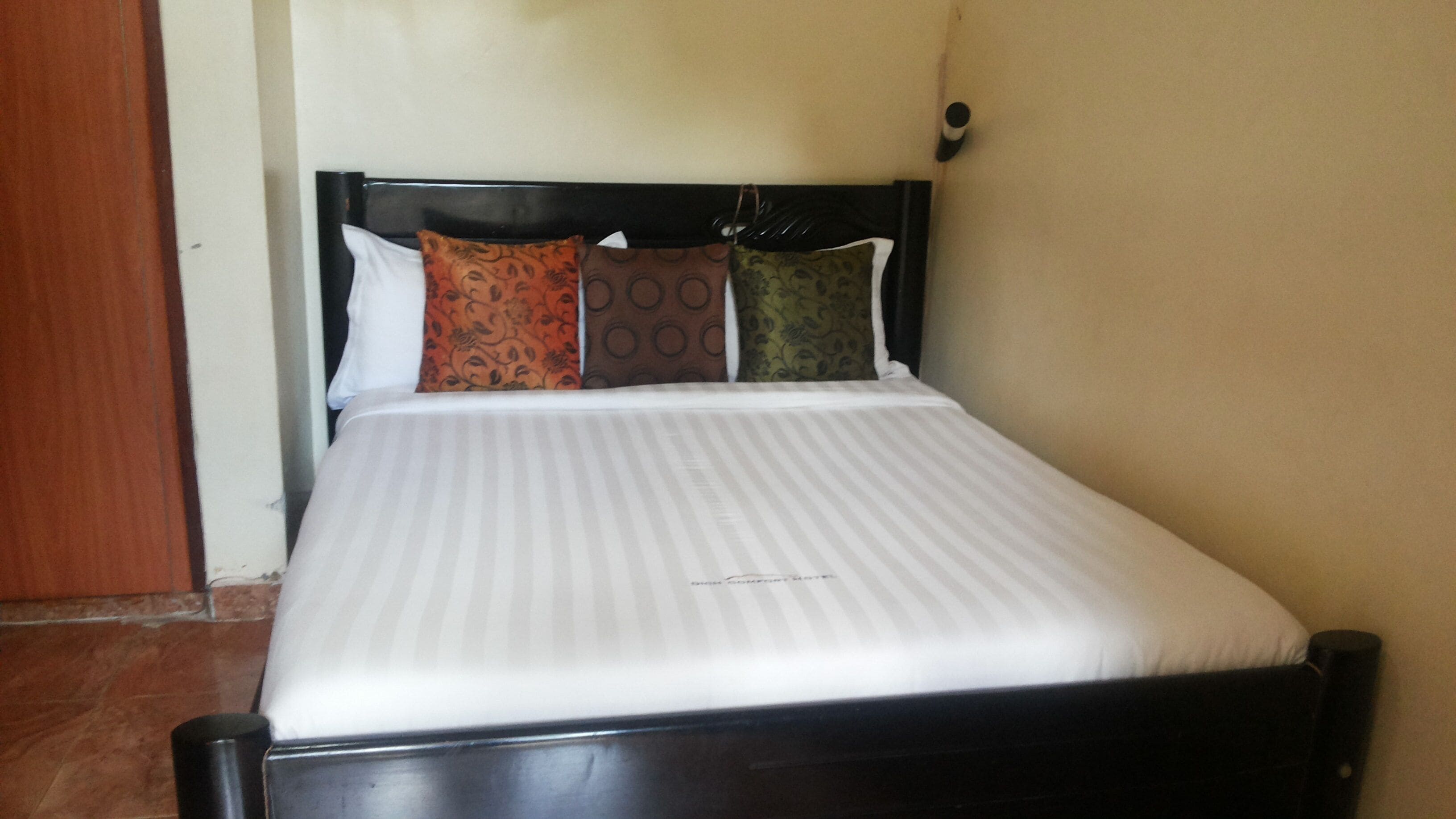 Una cama con colchón a rayas, cabecera oscura y tres almohadas estampadas.