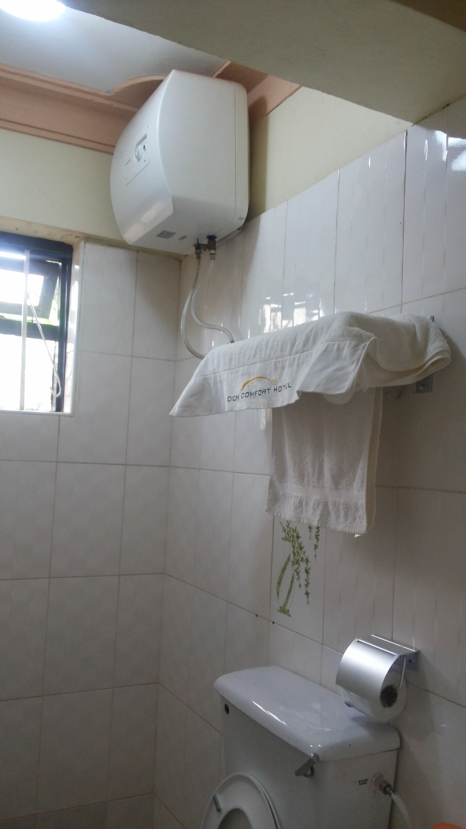 A bathroom with a toilet, a hand dryer, and a towel hanging on a rack.