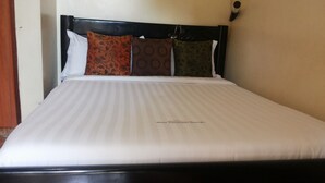 Cama bem arrumada com colcha branca e três almofadas estampadas.