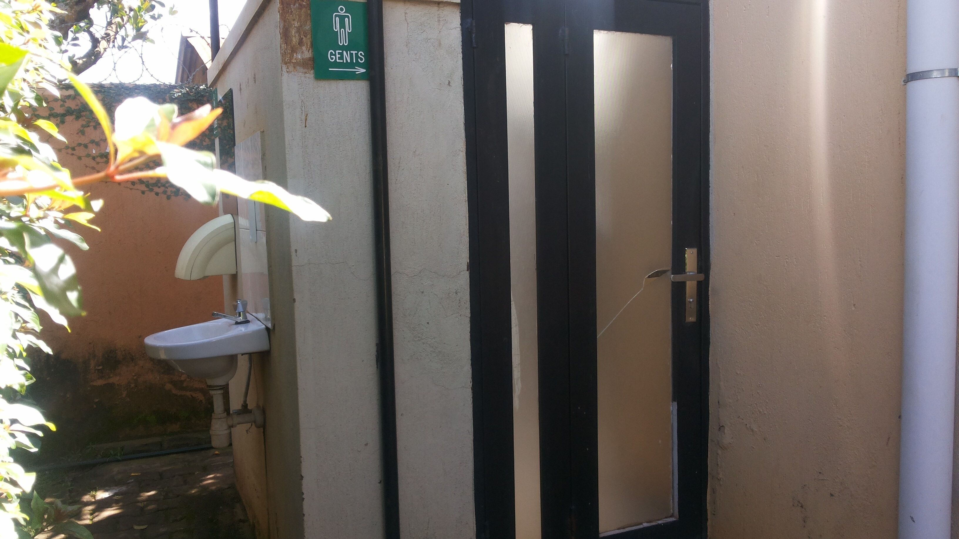 Casa de banho masculina com lavatório, espelho e porta com placa a indicar que é para homens.