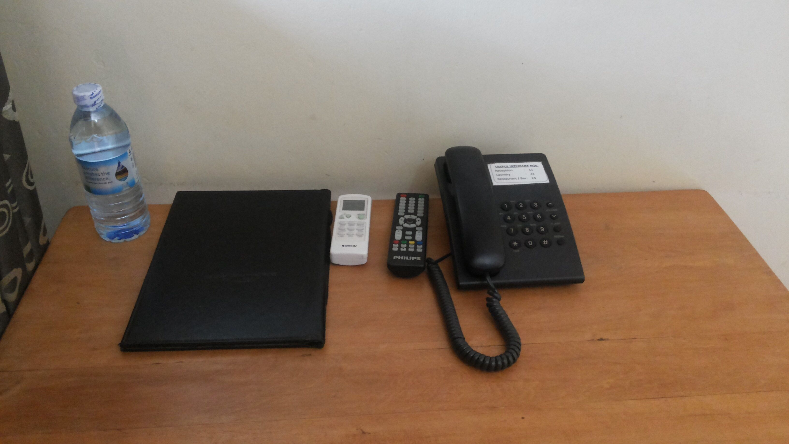 A wooden table with a black telephone, a Philips remote control, and a water bottle.
