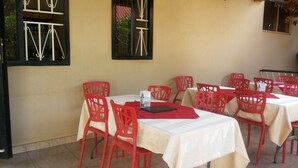 Uma área de refeições ao ar livre com cadeiras vermelhas e toalhas de mesa brancas.