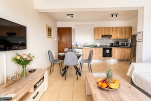 A modern hotel room with a dining area, kitchenette, and a TV mounted on the wall.