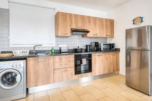 Eine moderne Küche mit Holzausbau, einem Edelstahlkühlschrank, einem Einbauofen, einer Waschmaschine und einer Mikrowelle.