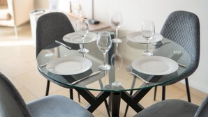 A modern dining area with a glass table surrounded by grey upholstered chairs. - Narcissos 'Nissi Beach' Apartment C3 (Ayia Napa)