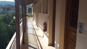 Ein überdachter Balkon mit Fliesenboden, ein an der Wand befestigter Feuerlöscher und eine Tür mit der Nummer 12.