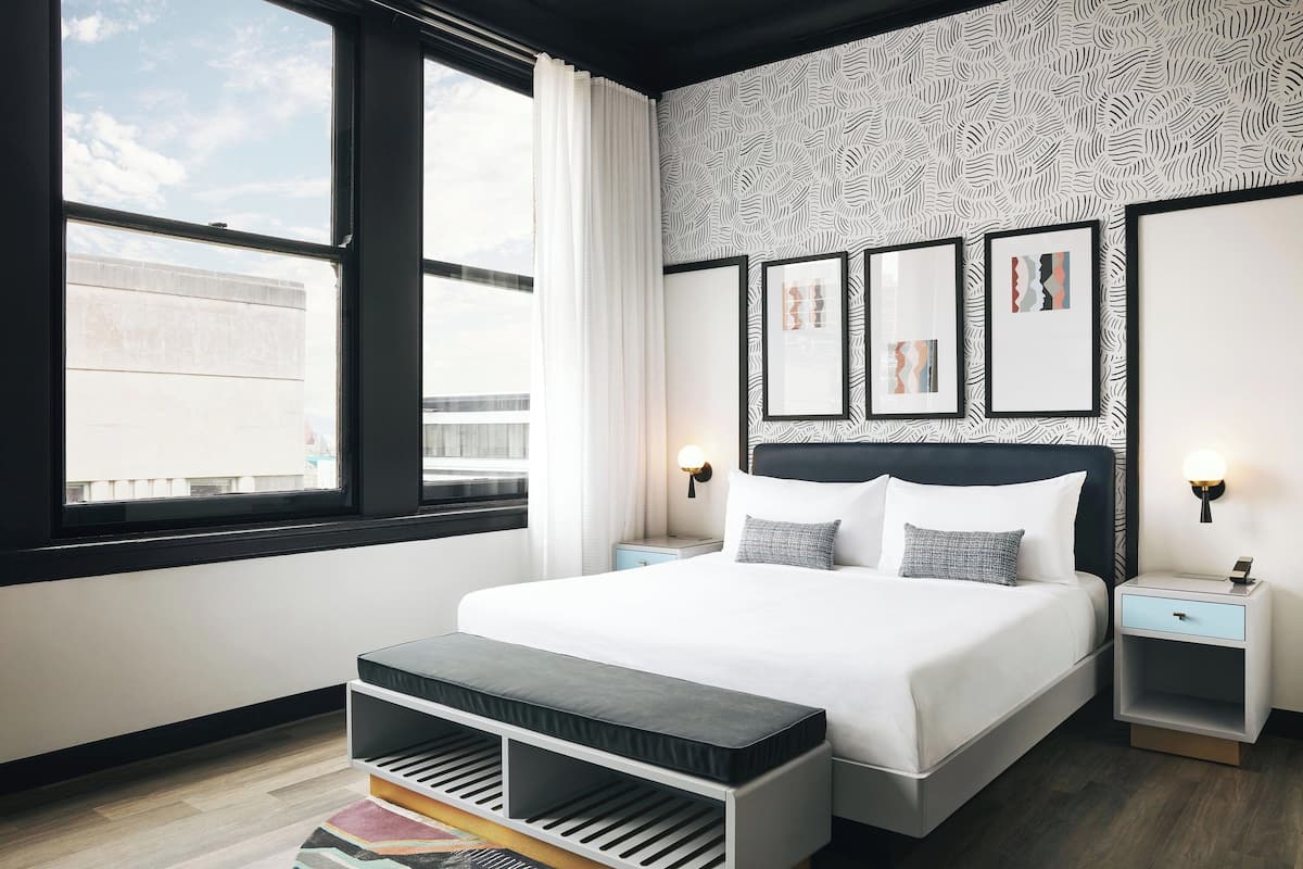 Moderni hotellihuone, jossa on suuri sänky, penkki, yöpöytä ja seinä, jossa on kehystettyjä kuvia.