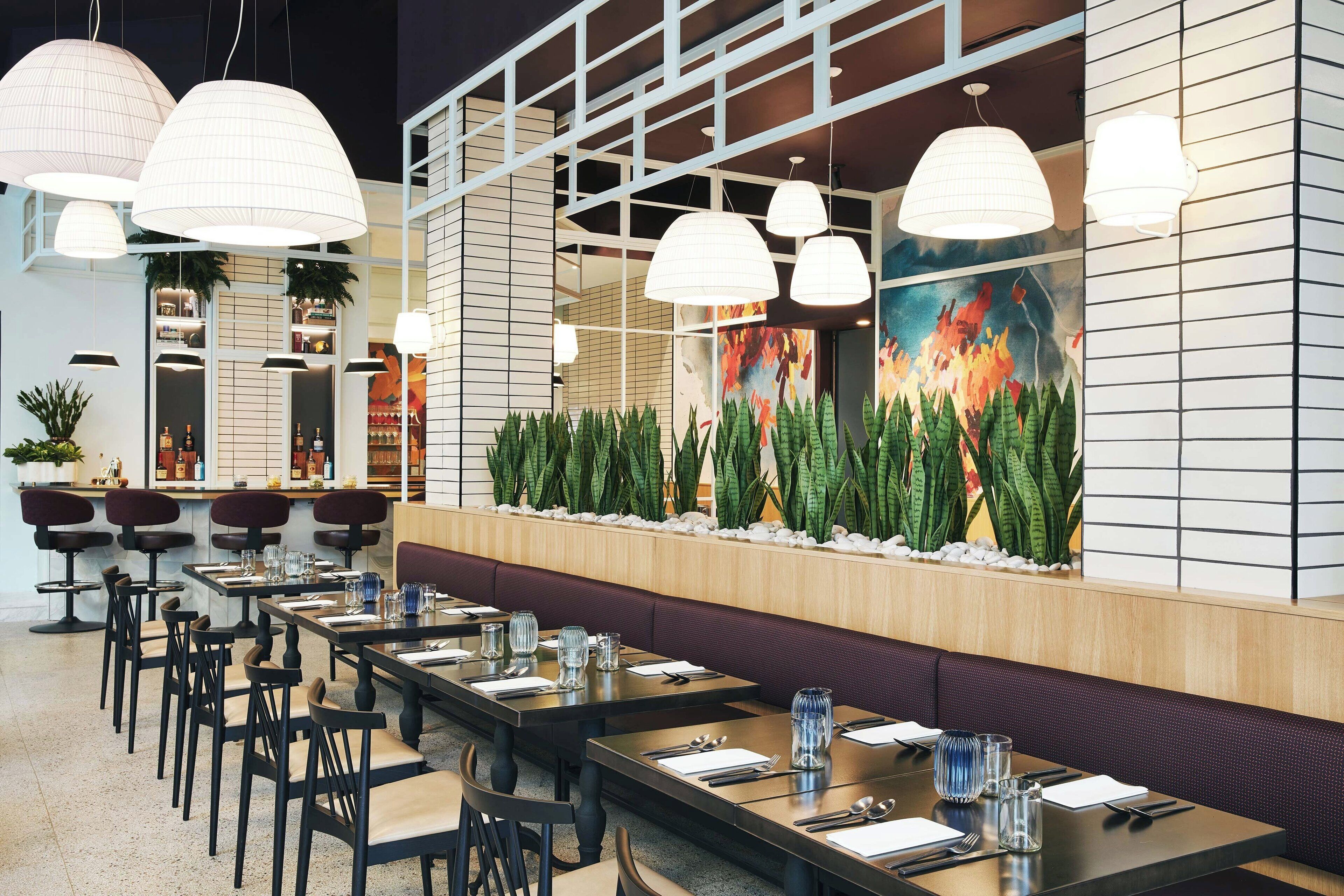 Un restaurante con mesas largas, sillas y lámparas colgantes.