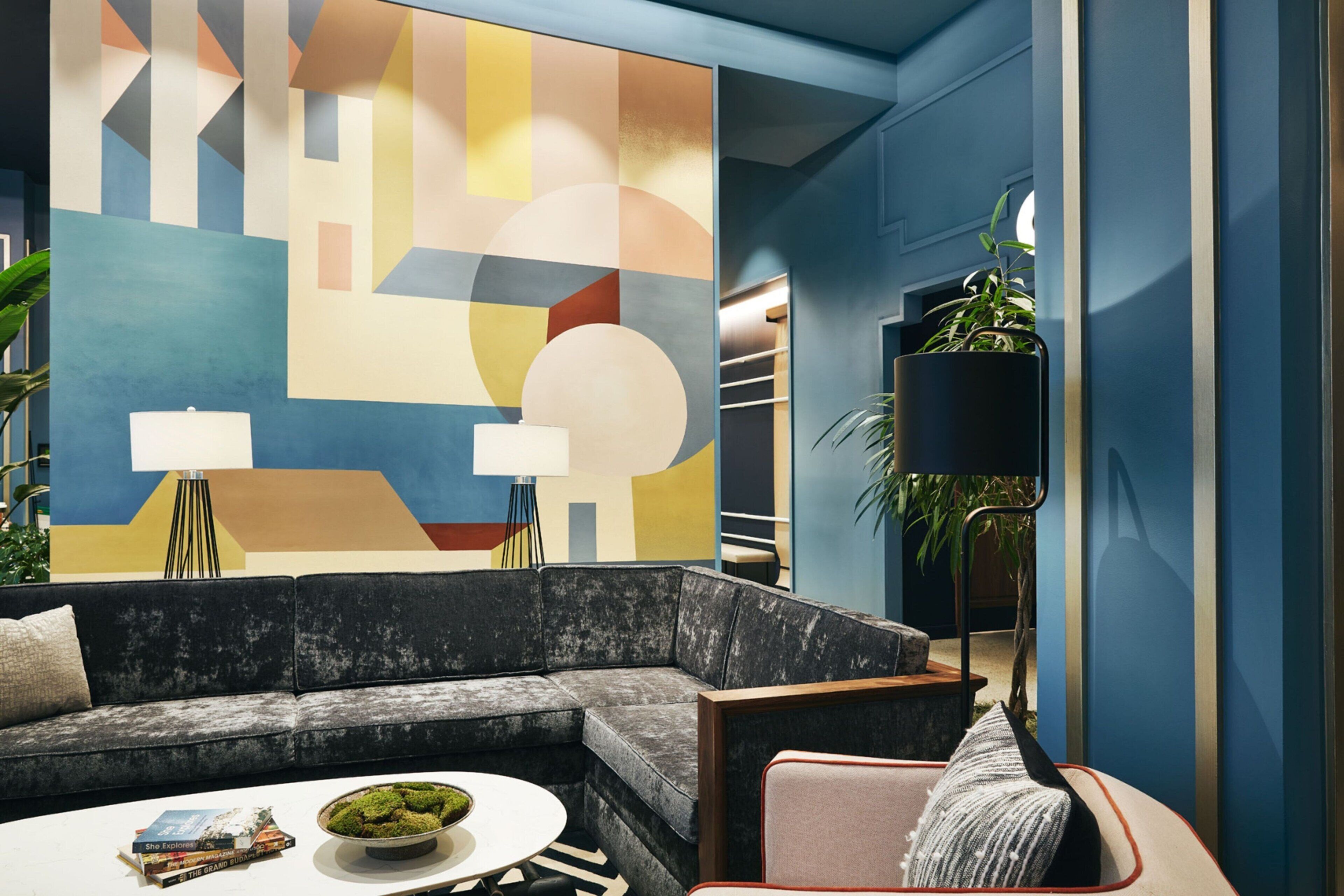 Una sala moderna con un sofá modular, una mesita de centro redonda con libros, una lámpara de pie y un cuadro abstracto grande en la pared.
